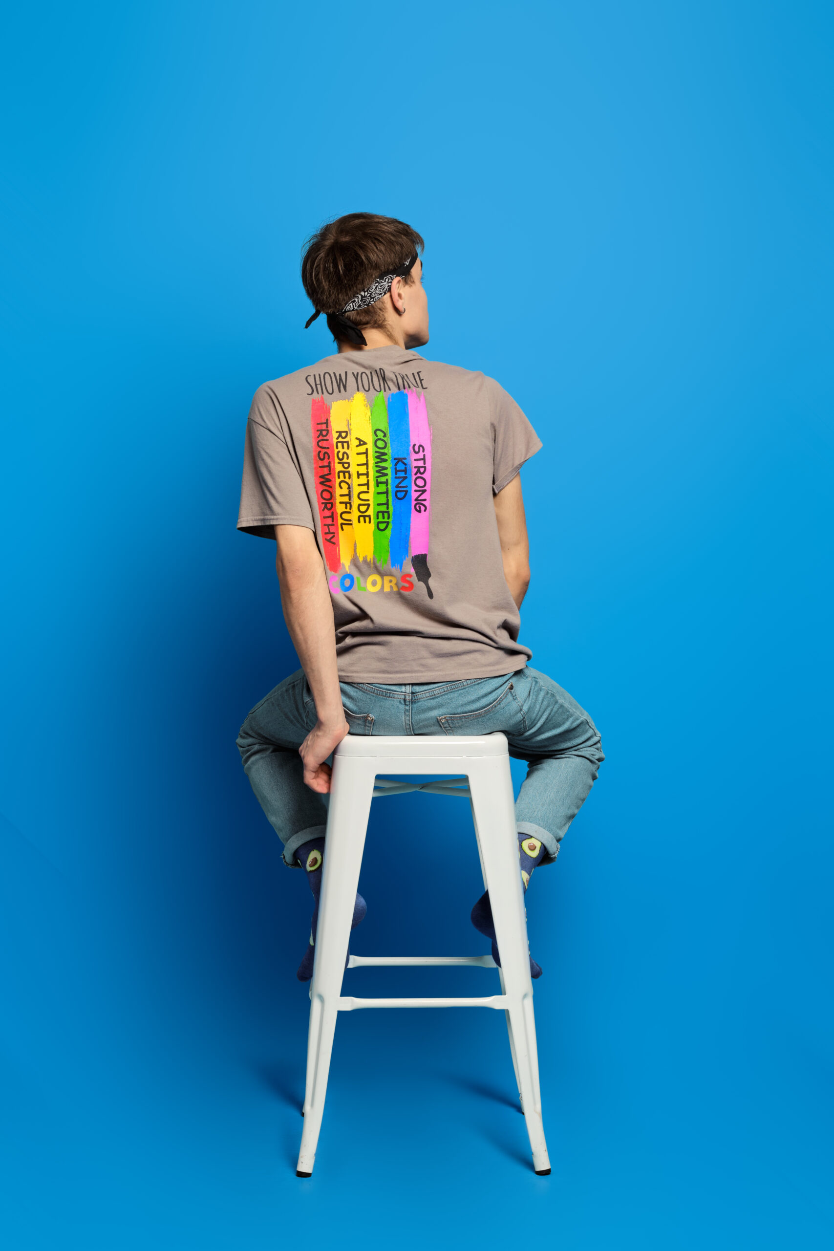 Unrecognizable adult person sits on tall stool in t-shirt with rainbow flag printed on back side. Concept of tolerant attitude to lgbt people.